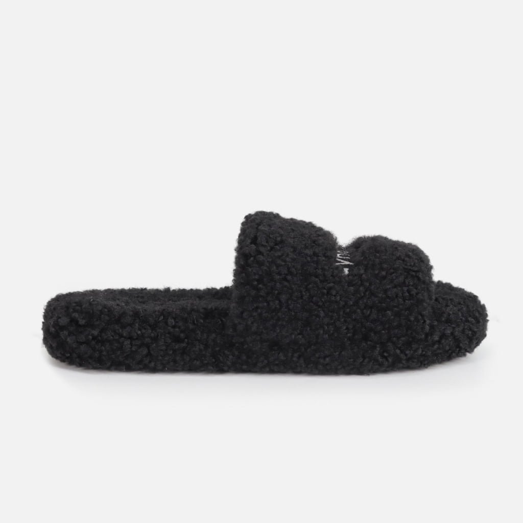 black slide slipper crafted from premium faux shearling fur, featuring a subtle custom label detail on the upper.